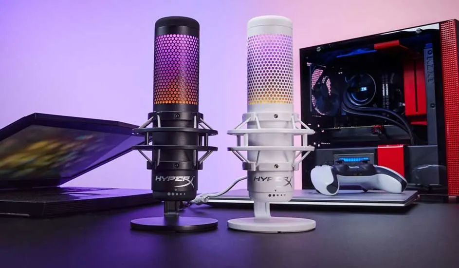 Deux microphones HyperX (noir, blanc) sur un bureau avec un ordinateur portable et une unité centrale. L'arrière-plan est violet.
