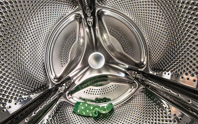 Een close-up van de binnenkant van een wasmachine, met een groen kledingstuk onderin.