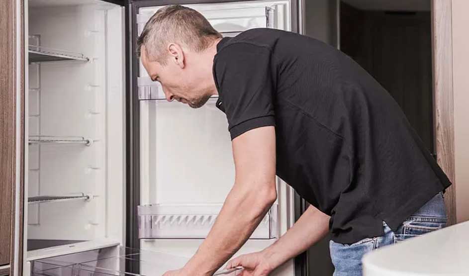 Un frigo blanc ouvert montre des étagères vides. L'intérieur est lumineux. Un meuble en bois est visible à gauche.