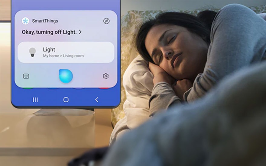 Femme dormant dans un lit, à côté d'un smartphone affichant l'application SmartThings et le message "Okay, éteindre la lumière".