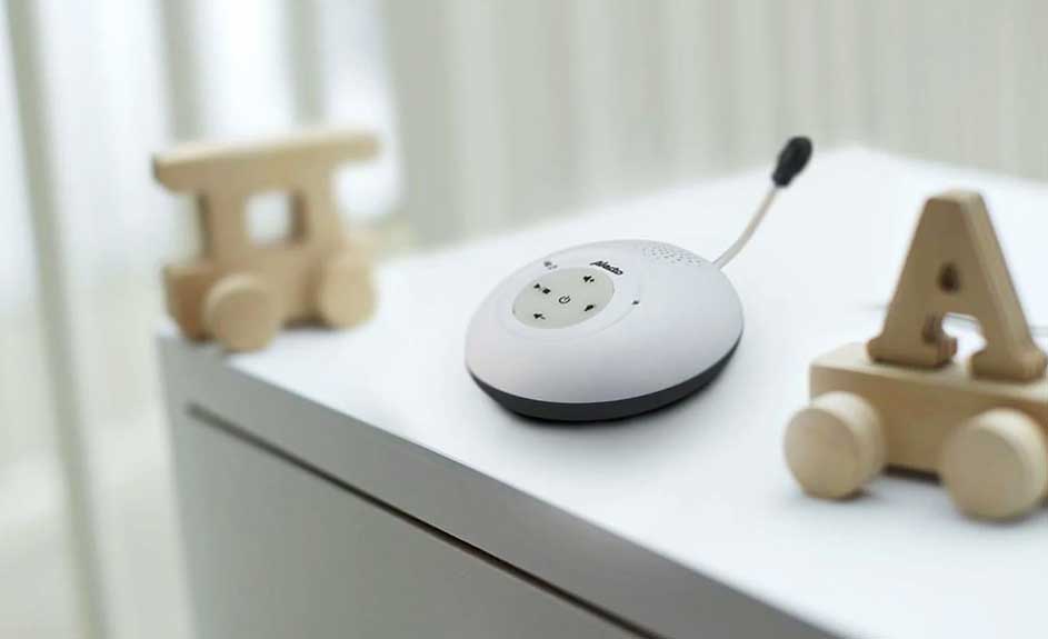 Un babyphone blanc avec des boutons est placé sur une table blanche à côté de jouets en bois.