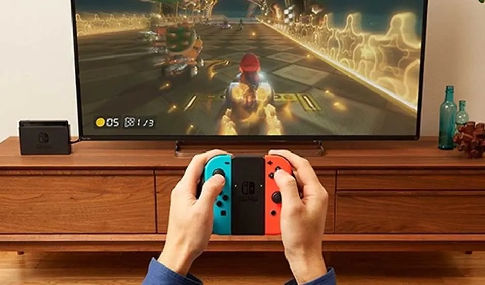 Someone is playing Mario Kart on a Nintendo Switch with Joy-Con controllers in front of a TV.