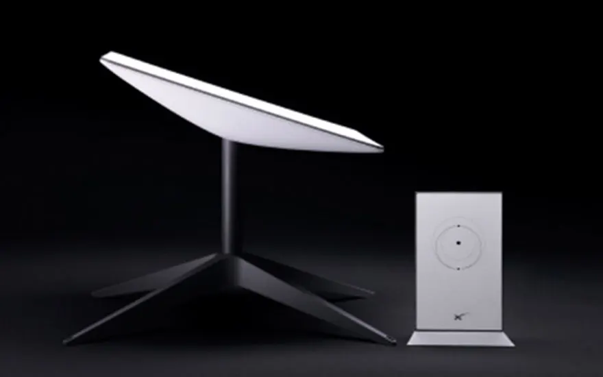 Un kit Starlink sur fond noir. Une antenne parabolique blanche sur un trépied noir, avec un routeur blanc à droite.