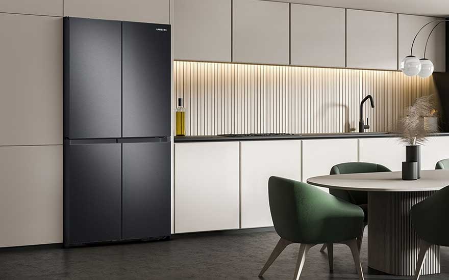 Zwarte Samsung koelkast in een keuken met witte kasten en een ronde tafel met groene stoelen.