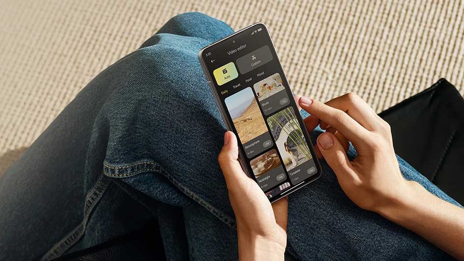 Iemand gebruikt een smartphone met een video-editor app op hun schoot, gekleed in een blauwe jeans. Op de achtergrond is een beige oppervlak te zien.