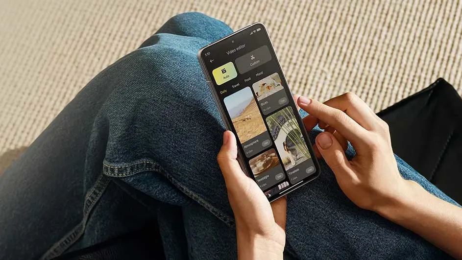 Une personne assise avec un jean bleu utilise un éditeur vidéo sur un smartphone. L'arrière-plan est un tapis beige.