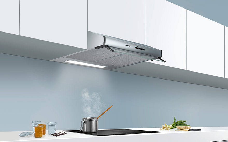 Een zilverkleurige dampkap boven een kookplaat met een stoompot, op een wit aanrecht in een keuken met blauwe wanden.