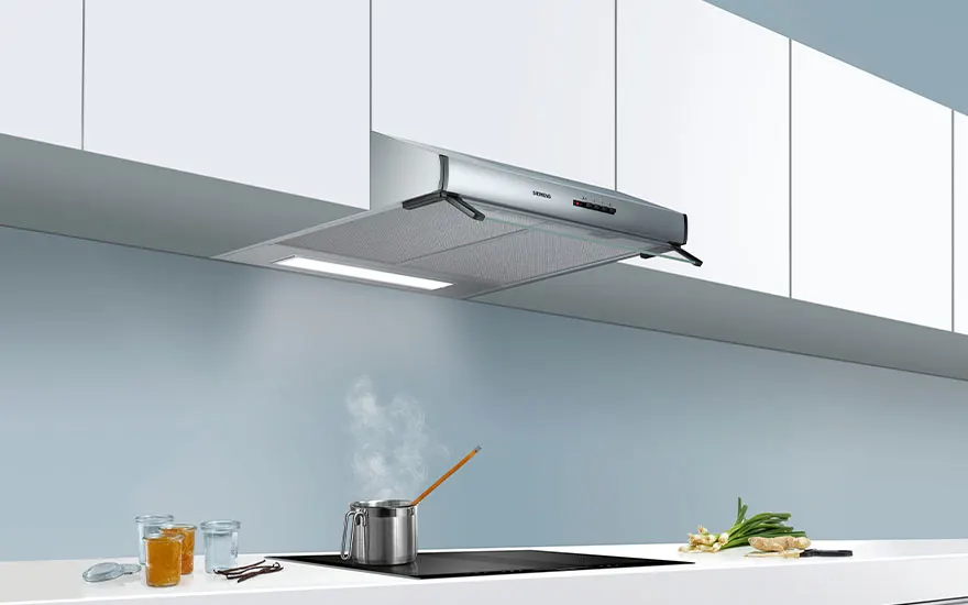 Een zilverkleurige dampkap boven een kookplaat met een stoompot, op een wit aanrecht in een keuken met blauwe wanden.