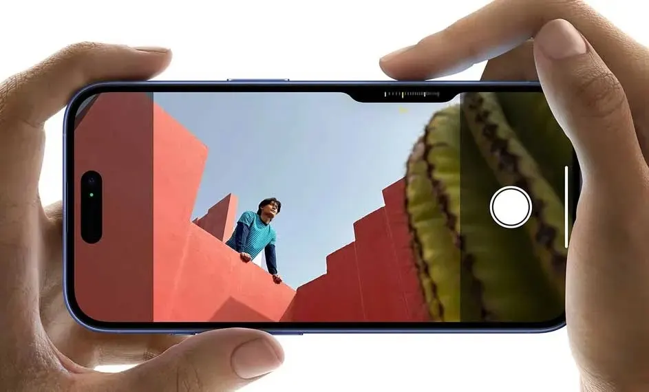 Two hands hold an Apple iPhone; the screen shows the camera app with red stairs and a person in a blue shirt.