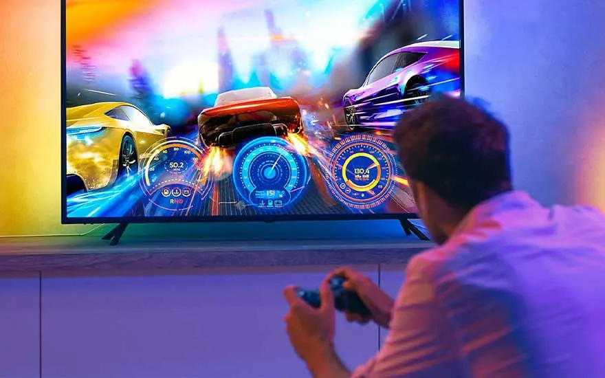 Un écran TV affiche un jeu de course automobile coloré avec des compteurs bleus. Le téléviseur est sur un meuble blanc.