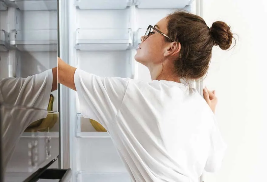 Une personne ouvre un réfrigérateur blanc. Des bananes sont visibles à l'intérieur.