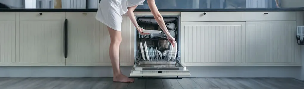 A dishwasher stands open in a kitchen with light grey cabinets and a dark countertop. Dishes fill the dishwasher racks.