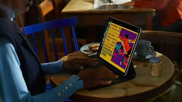 Een tablet staat op een houten tafel naast een kop en een koekje. Het scherm toont een kleurrijke afbeelding.