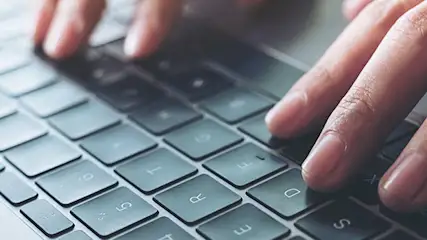 Mains tapant sur un clavier d'ordinateur portable gris. Les doigts sont positionnés sur les touches. Clavier moderne.