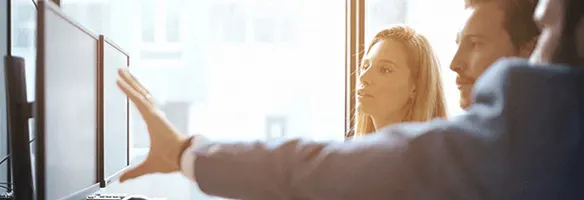Deux écrans d'ordinateur noirs sont placés devant une fenêtre lumineuse dans un bureau. Une main tendue vers les écrans.