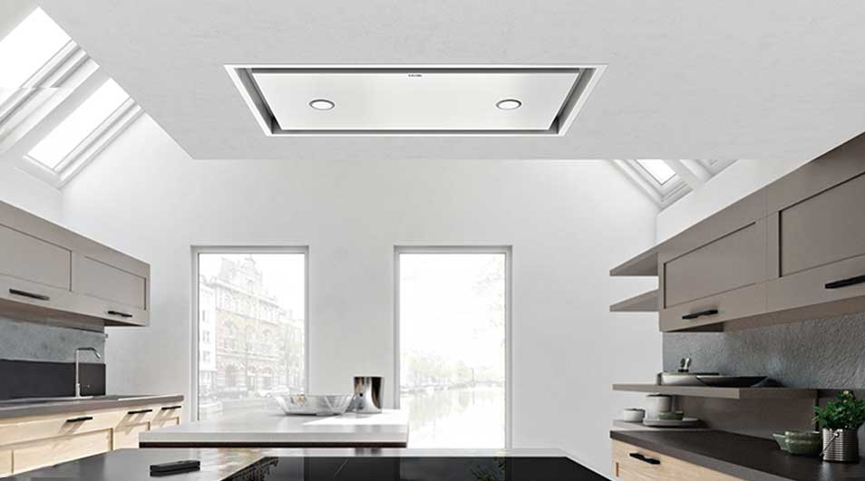 Cuisine moderne et lumineuse avec hotte intégrée au plafond blanc, fenêtres et armoires grises.