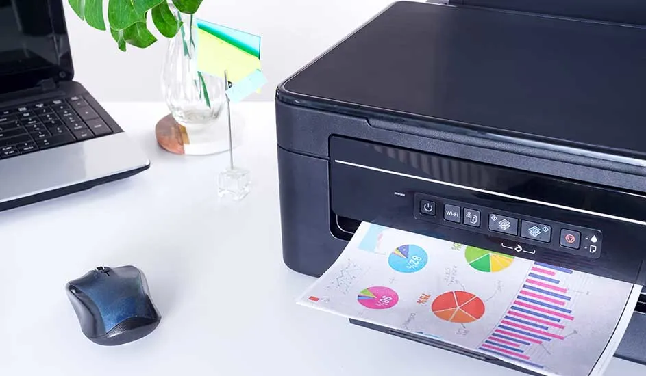 Een zwart-grijze printer print een blad met kleurrijke grafieken op een witte tafel. Een laptop en muis zijn zichtbaar.