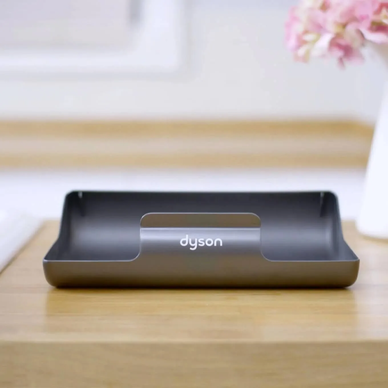 Support Dyson gris sur table en bois. Fleurs roses floues en arrière-plan.