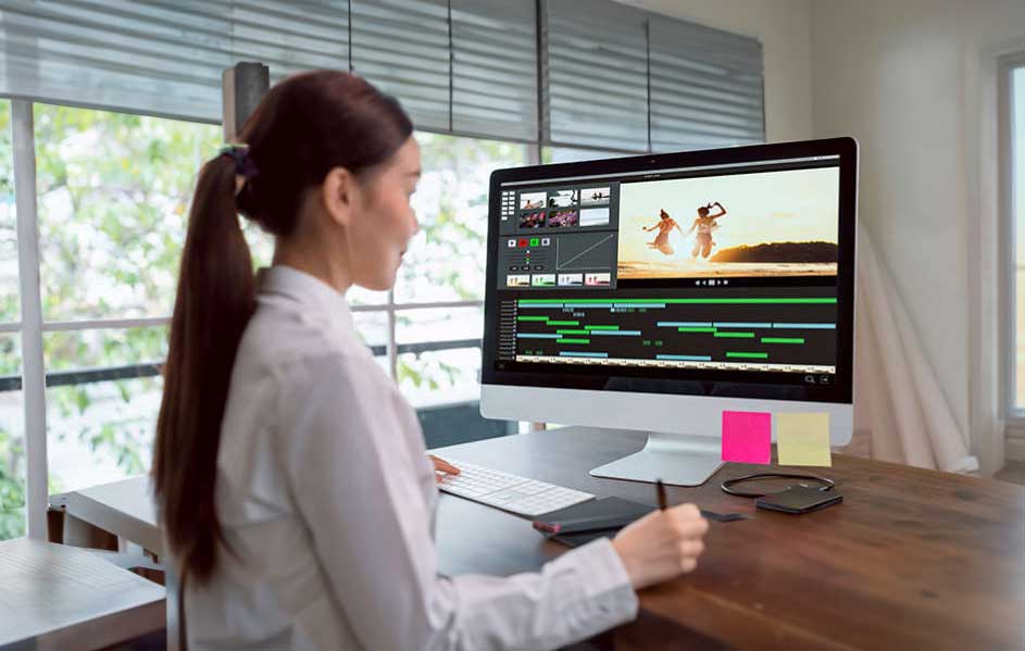 Een computer toont videobewerkingssoftware op een houten bureau met een toetsenbord en tekentablet voor een raam.