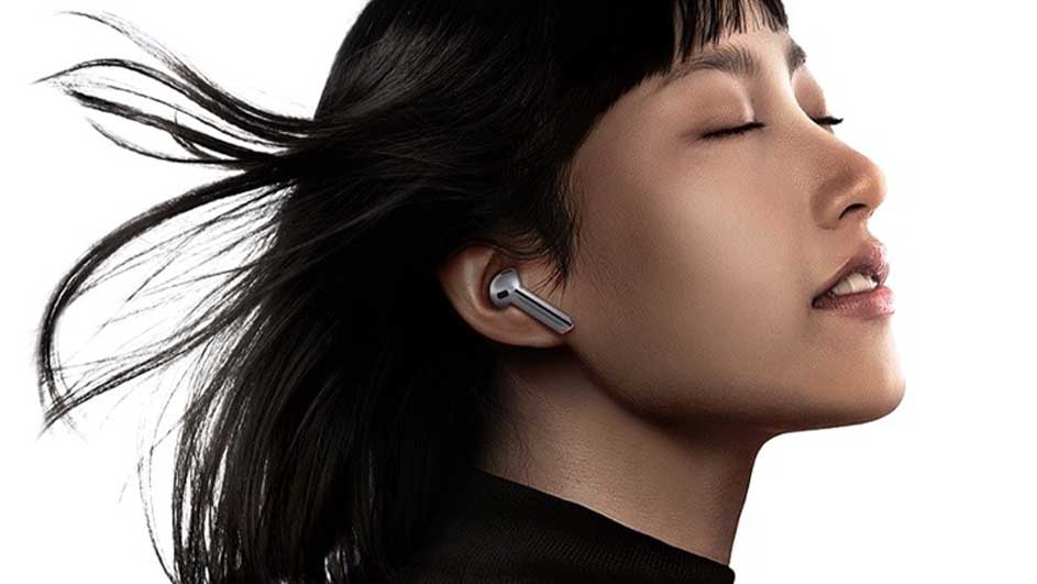 Une personne porte un écouteur argenté. L'arrière-plan est blanc.