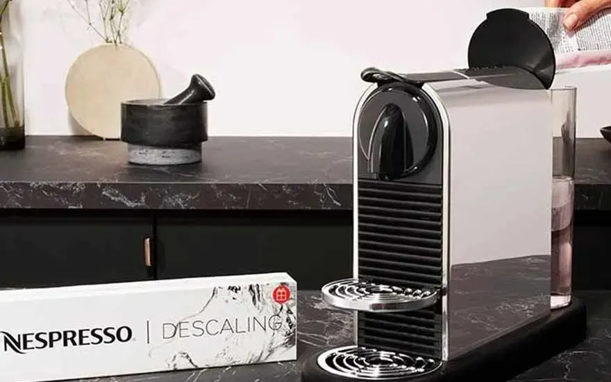 Een Nespresso-apparaat staat op een marmeren aanrecht, naast een ontkalkingskit en een vijzel.