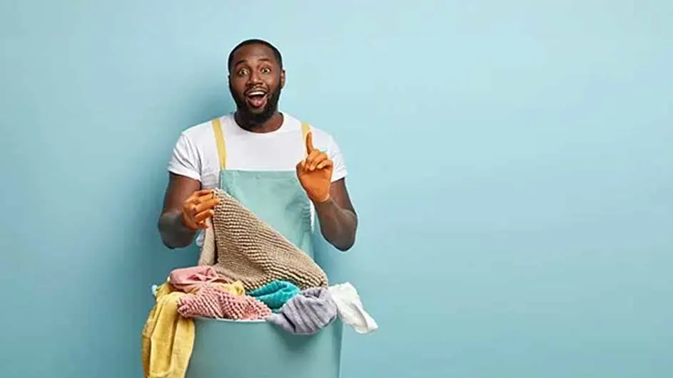 Un panier à linge bleu rempli de vêtements colorés sur fond bleu. Il y a un tablier bleu clair.