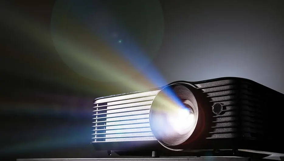 Een zwarte projector straalt licht uit tegen een grijze achtergrond. De lichtstralen zijn blauw, groen en wit.