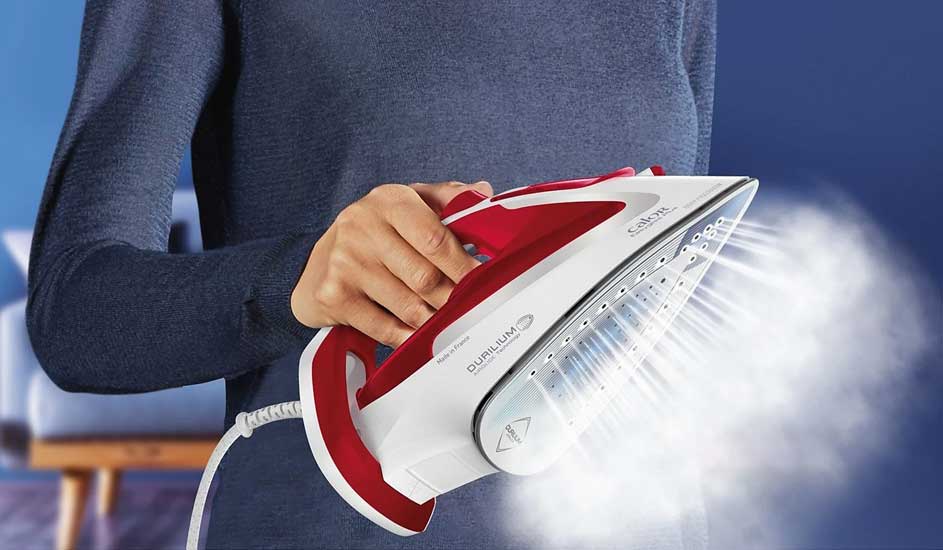 Un fer à repasser blanc et rouge émet de la vapeur. Le fer est tenu par une main. Fond bleu.