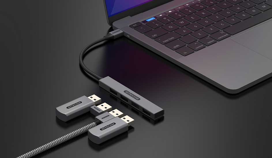 Un ordinateur portable gris connecté à un hub USB gris avec des ports USB supplémentaires sur une surface noire.