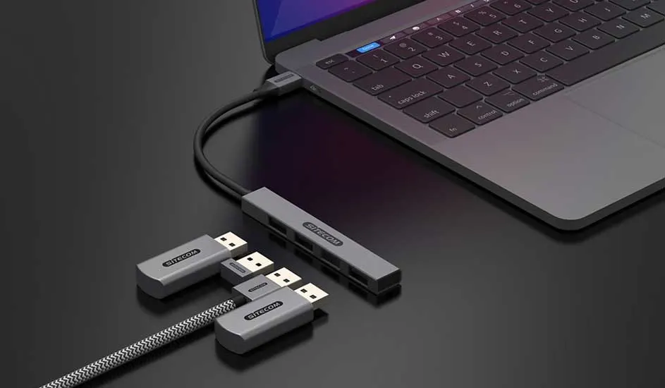 Een grijze laptop is aangesloten op een grijze USB-hub met meerdere USB-connectoren op een zwarte tafel.