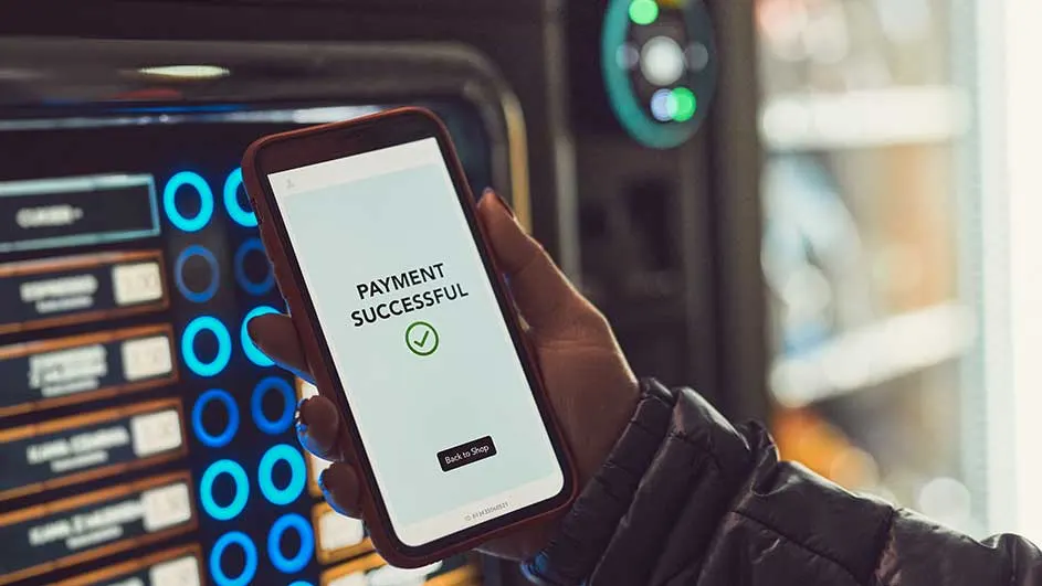 Un téléphone affiche "Paiement réussi" devant un distributeur avec des lumières bleues.