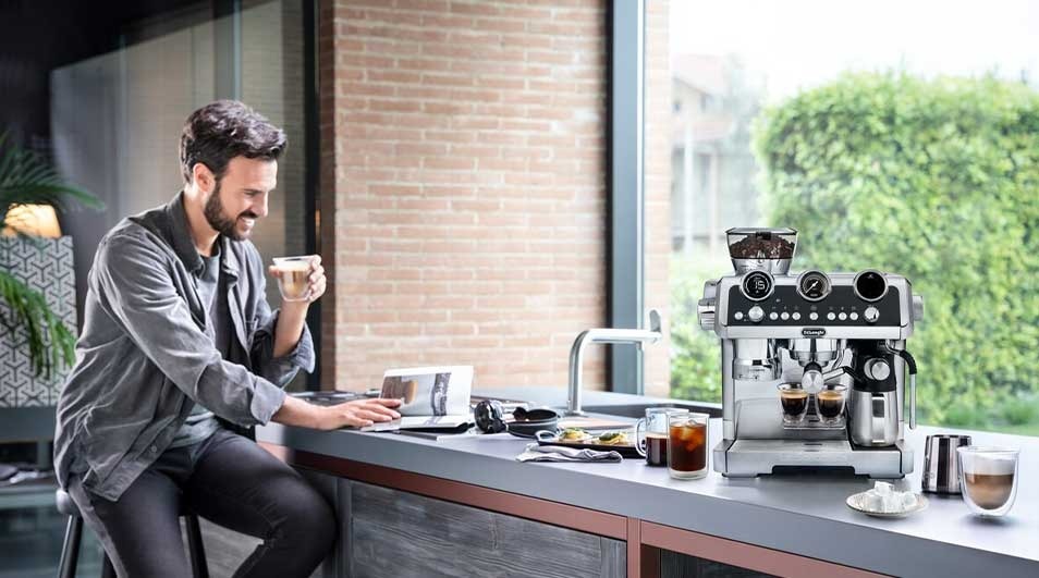 A relaxed man enjoys coffee at a sleek kitchen counter, beside a shiny espresso machine pouring two rich shots.