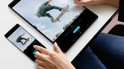 Deux écrans affichent une personne faisant du skateboard sur fond de ciel. Une main utilise un stylet sur la tablette.
