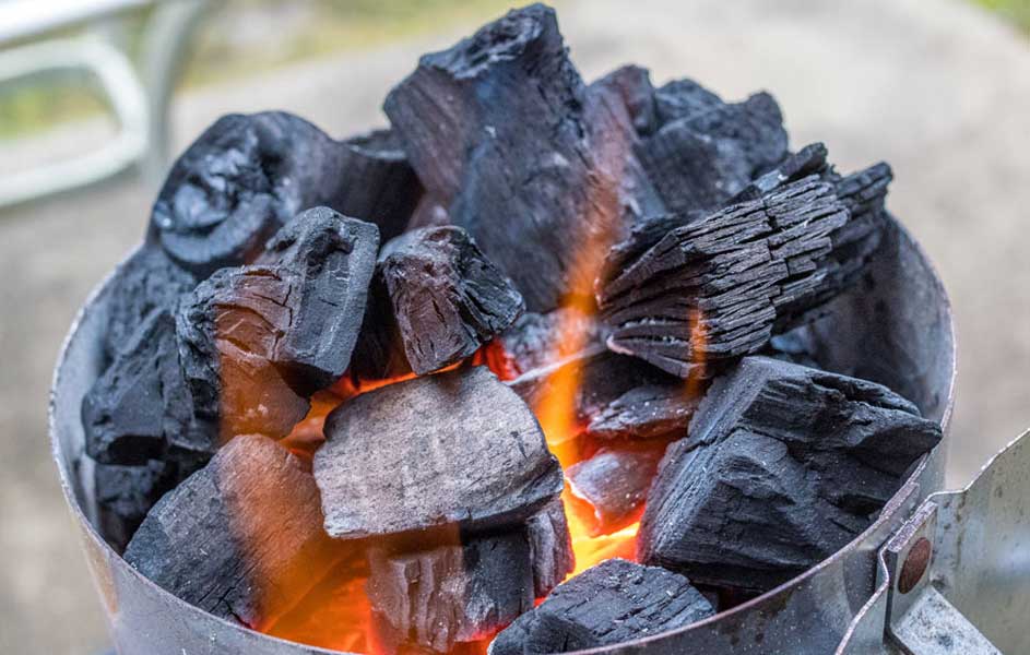 Un récipient métallique rempli de morceaux de charbon de bois en train de brûler avec des flammes orange.