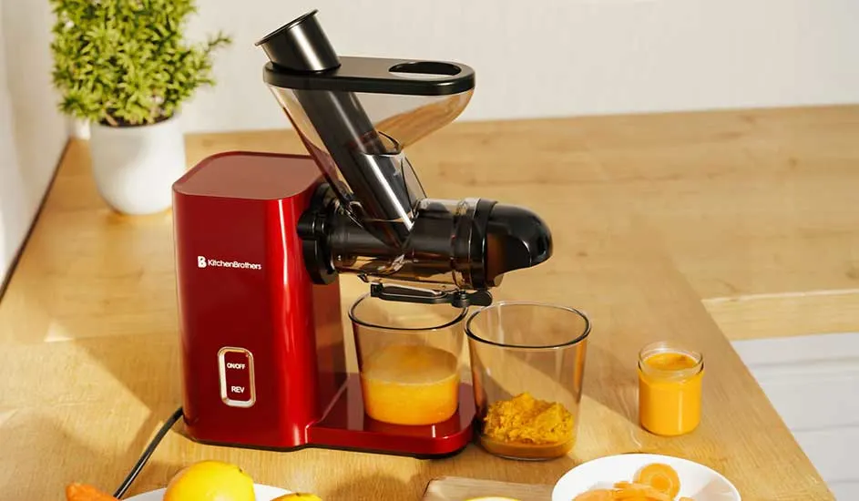 Une centrifugeuse presse des morceaux de fruits en jus frais, versé dans un verre, la pulpe est recueillie à part dans un récipient transparent.
