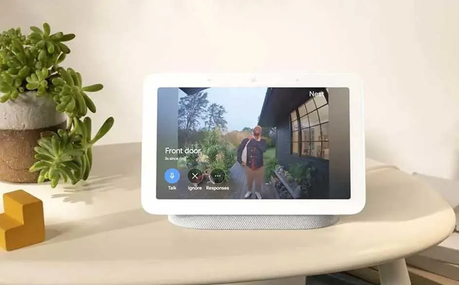 Un écran affiche une sonnette vidéo Nest sur une table blanche. Une plante verte et un jouet jaune sont à côté.