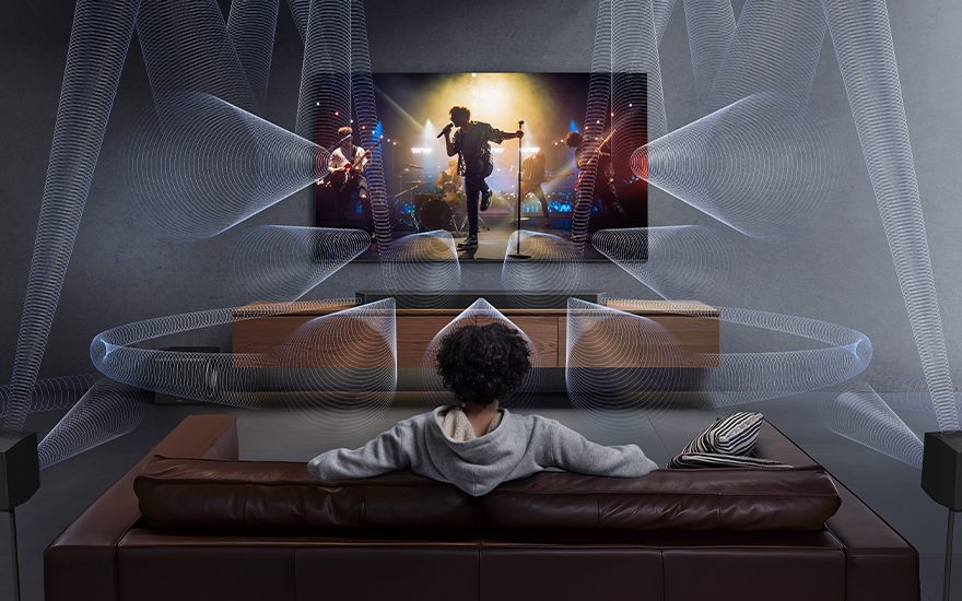 Un salon avec un canapé en cuir marron, une télévision montrant un concert et des enceintes avec des ondes sonores bleues.