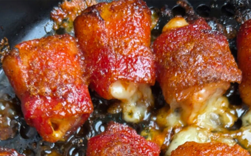 Gros plan sur des bouchées apéritives caramélisées dans un plat noir, avec du fromage fondu visible.