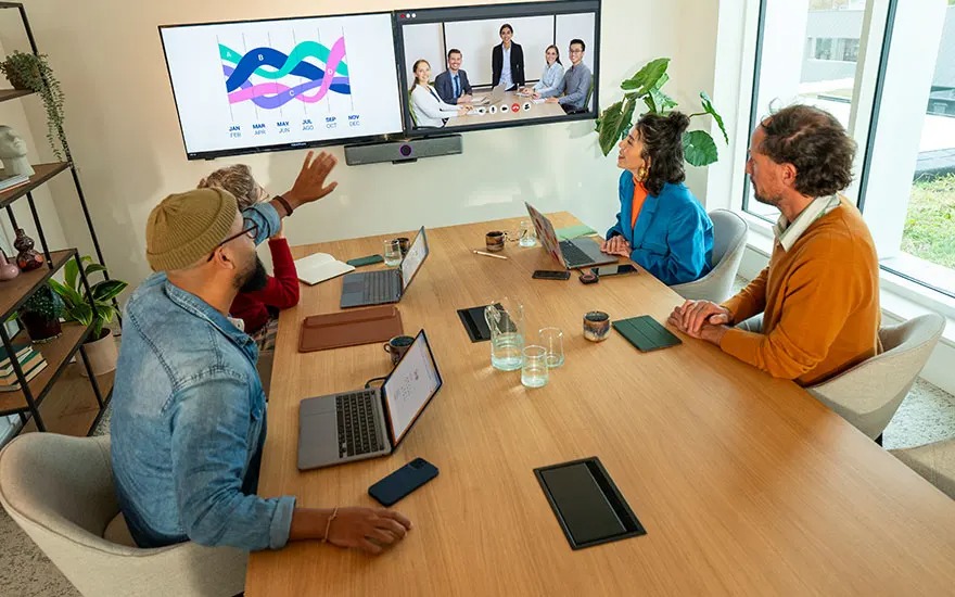 Three young people at a table with laptops smile, relaxed atmosphere, ready to collaborate in a modern meeting room.