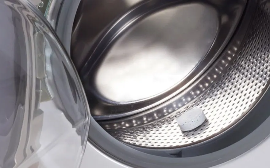 Vue intérieure d'un lave-linge gris avec une pastille blanche sur le tambour perforé. La porte est ouverte.