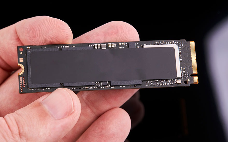 Une main tient une carte SSD noire avec connecteurs dorés sur un fond noir.