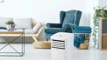 Domo mobiele airconditioner staat in een lichte, moderne woonkamer met een bank, fauteuil en planten; merk Domo goed zichtbaar.