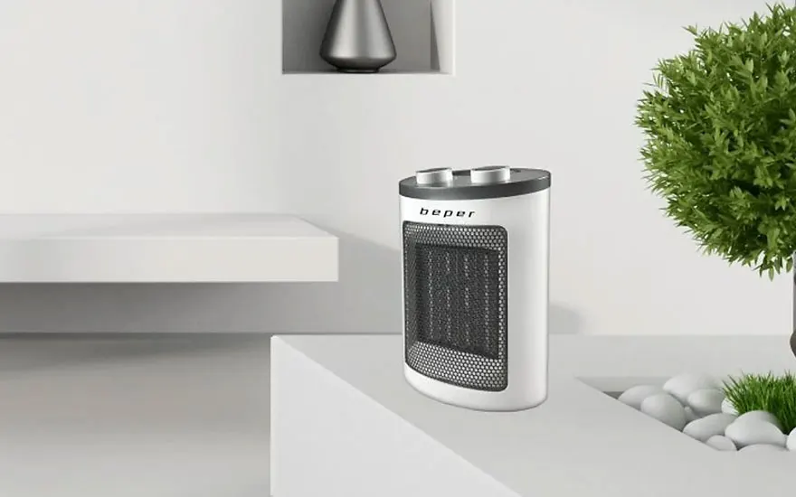 Un radiateur électrique blanc est posé sur une surface blanche avec une grille noire. Un arbuste vert est visible à droite.