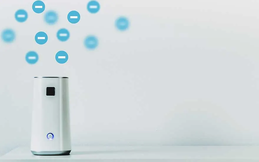 Un petit ioniseur d’air blanc posé sur une table libère des symboles d’ions négatifs bleus, illustrant la neutralisation discrète poussières et odeurs.