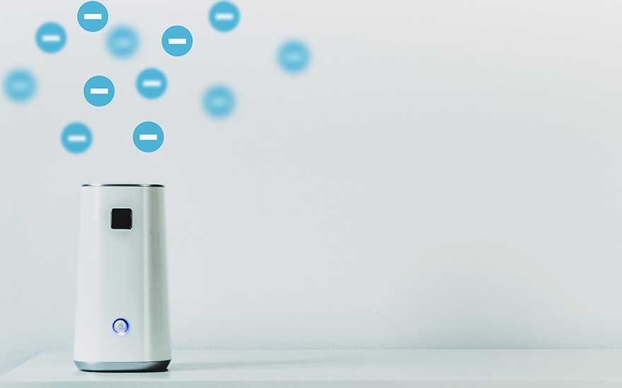 Een compacte witte ionisator staat op een tafel en stuurt blauwe negatieve ionen de lucht in, om stof, pollen en geurtjes onzichtbaar te neutraliseren.