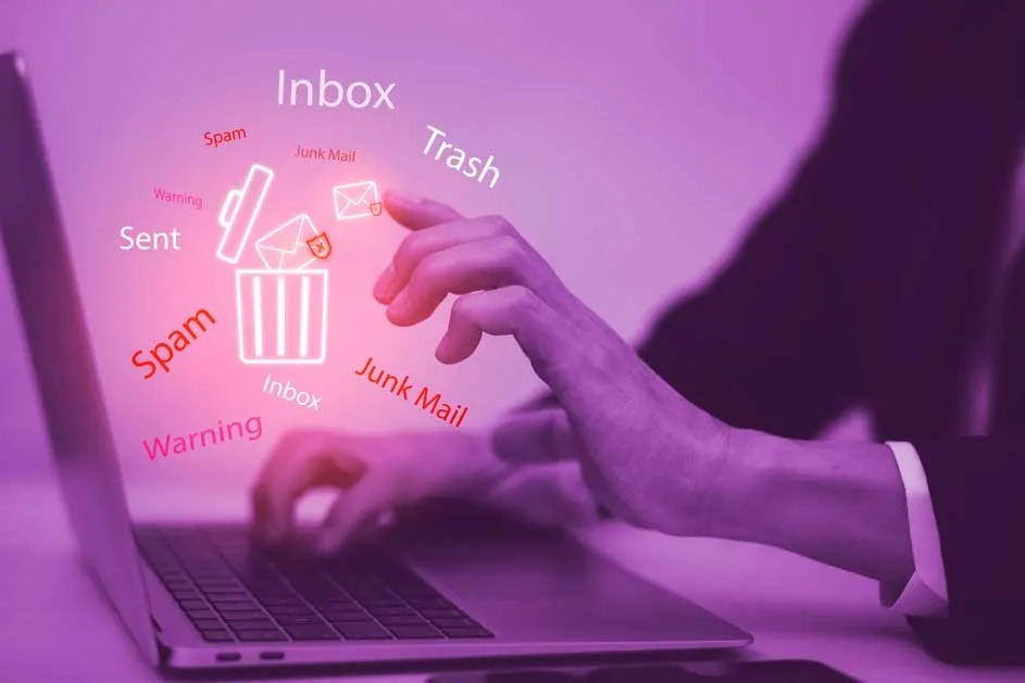 Een laptop met e-mailgerelateerde woorden zoals "Inbox", "Spam" en een prullenbak-icoon. Twee handen typen op het toetsenbord.
