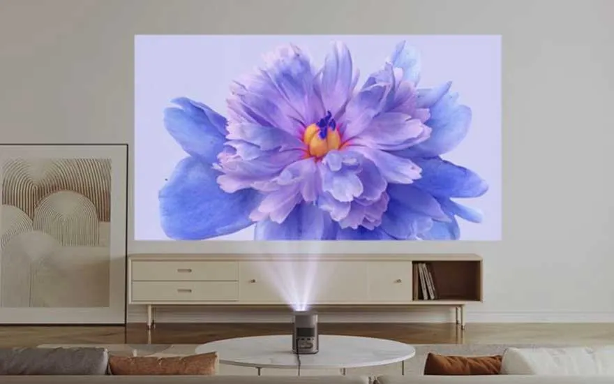 Un projecteur diffuse une fleur bleue sur un mur blanc, au-dessus d'un meuble beige. Un tableau est visible à gauche.