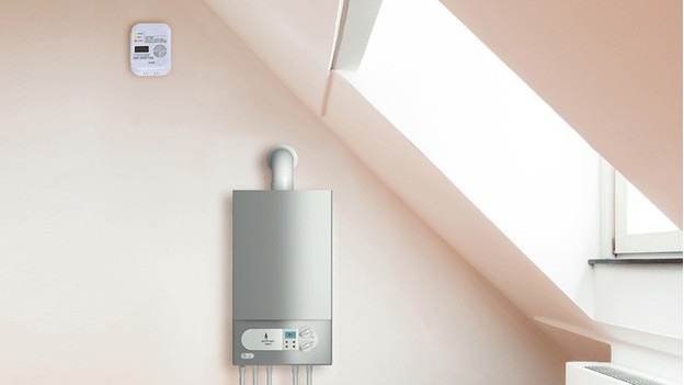 Appareil de chauffage gris sur mur beige près d'un détecteur et d'une fenêtre de toit.