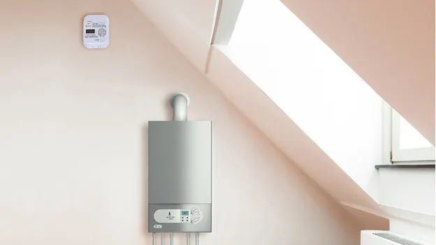 Appareil de chauffage gris sur mur beige près d'un détecteur et d'une fenêtre de toit.