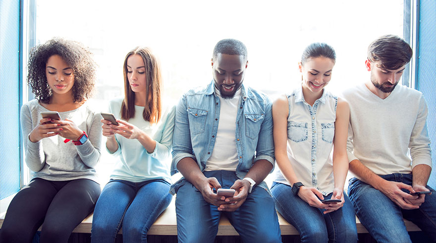 Cinq personnes assises près d'une fenêtre bleue, utilisant des smartphones. Vêtements variés, jeans et hauts décontractés.